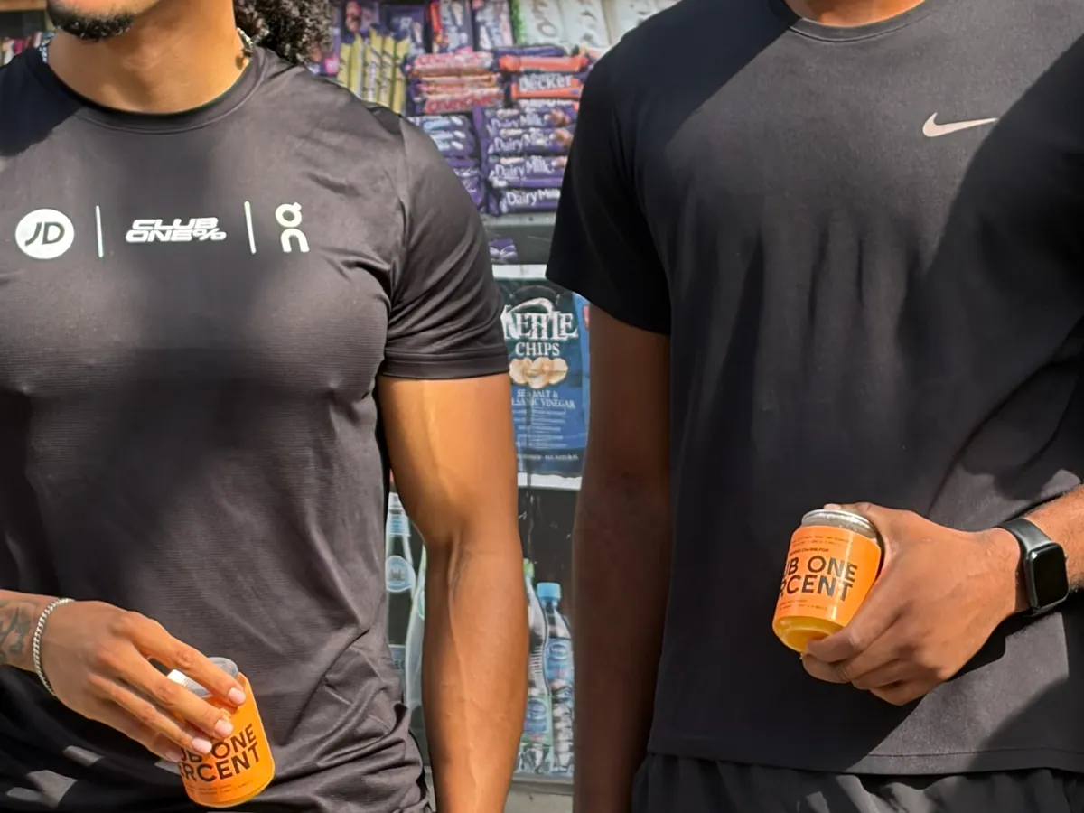 Two Club One Percent members in training kit hold orange cans with a custom Club One Percent label