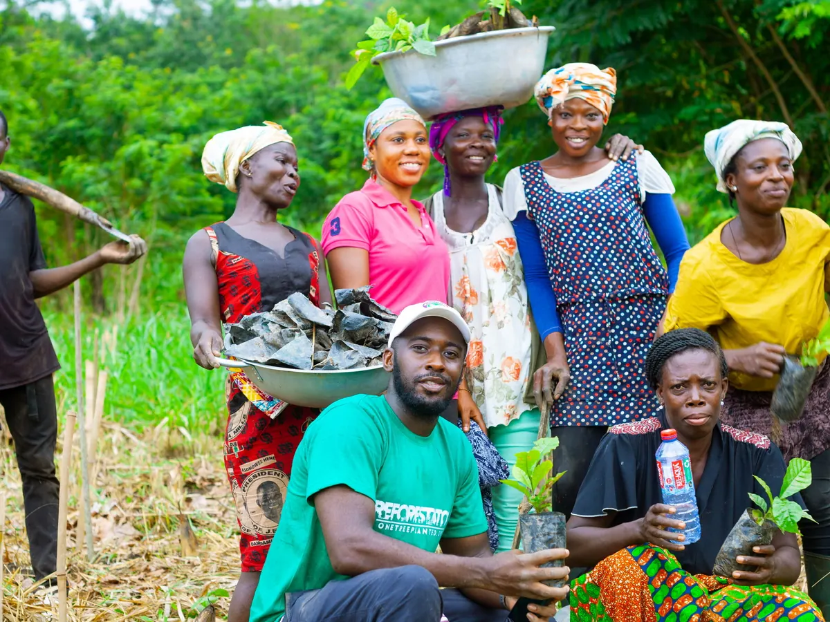 Farmers in Ghana smile for the camera holding young seedlings ready for planting
